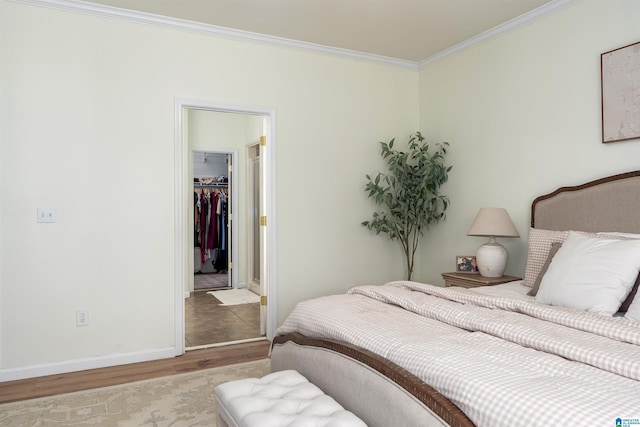 bedroom with a spacious closet, crown molding, baseboards, wood finished floors, and a closet