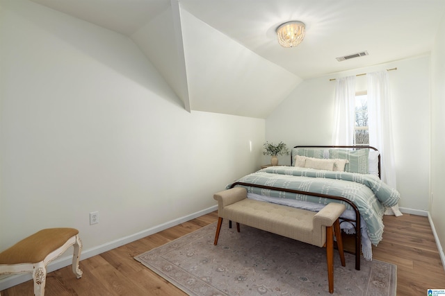 bedroom with lofted ceiling, wood finished floors, visible vents, and baseboards