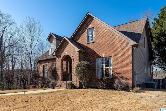 traditional-style home featuring central air condition unit, brick siding, roof with shingles, and a front lawn