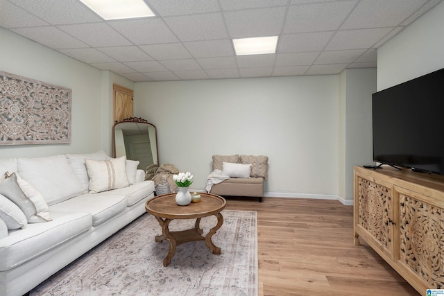 living area with light wood-style flooring, a paneled ceiling, and baseboards