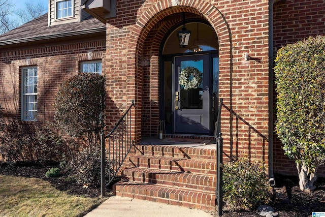 doorway to property with brick siding and a shingled roof