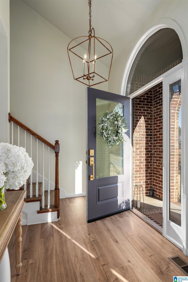 entryway with visible vents, stairway, an inviting chandelier, and wood finished floors