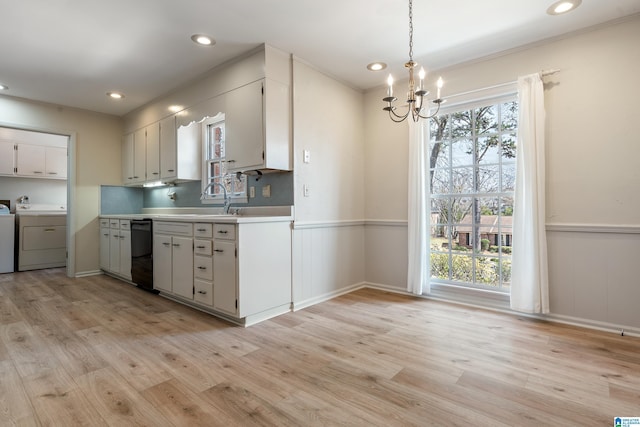 kitchen featuring light wood-type flooring, a wainscoted wall, black dishwasher, and washer and clothes dryer