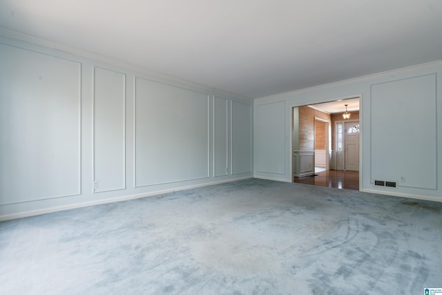 carpeted spare room with visible vents, ornamental molding, and a decorative wall