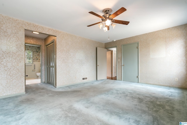 carpeted empty room with wallpapered walls, a ceiling fan, and visible vents