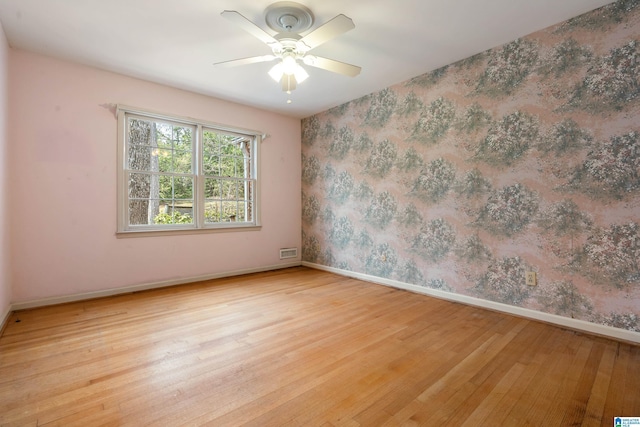 unfurnished room with visible vents, a ceiling fan, wood finished floors, wallpapered walls, and baseboards