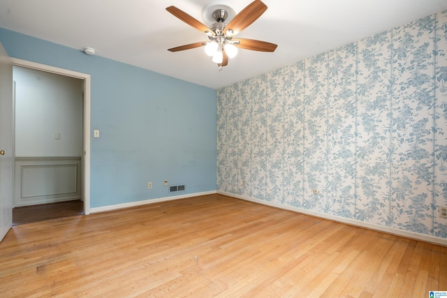 empty room featuring hardwood / wood-style floors, a ceiling fan, visible vents, baseboards, and wallpapered walls