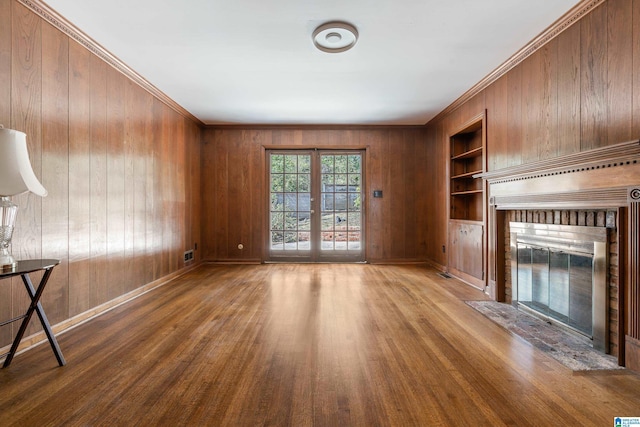 unfurnished living room with built in features, wood finished floors, french doors, baseboards, and a brick fireplace