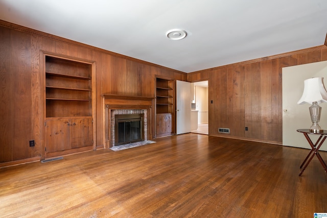 unfurnished living room featuring wooden walls, a brick fireplace, built in shelves, and wood finished floors