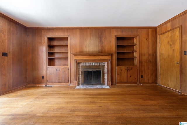 unfurnished living room with built in shelves, a brick fireplace, wood finished floors, and wood walls