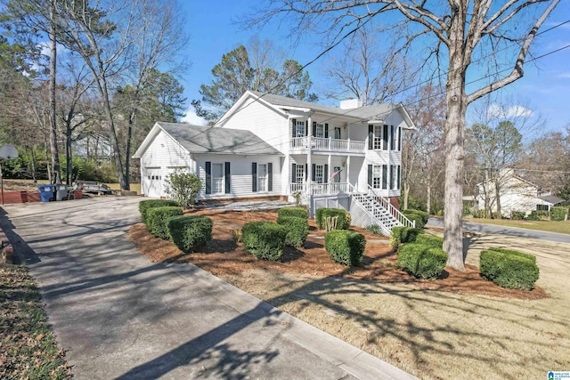 view of front facade with driveway, a balcony, a chimney, an attached garage, and covered porch