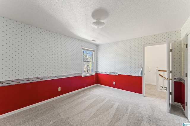 carpeted spare room with a textured ceiling, baseboards, visible vents, and wallpapered walls