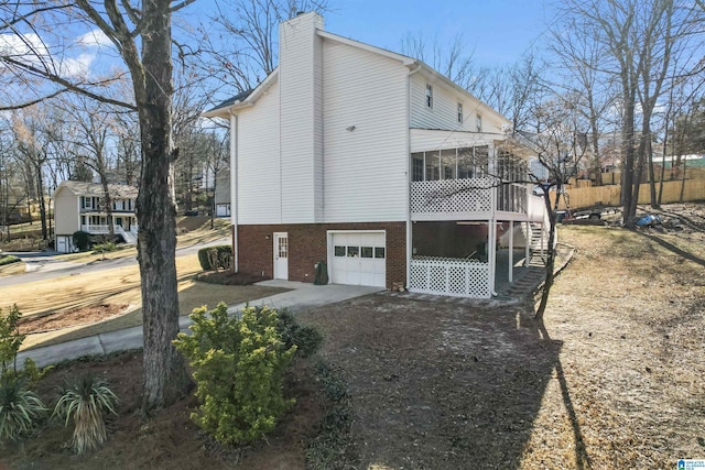 view of side of home with an attached garage, brick siding, a sunroom, driveway, and a chimney