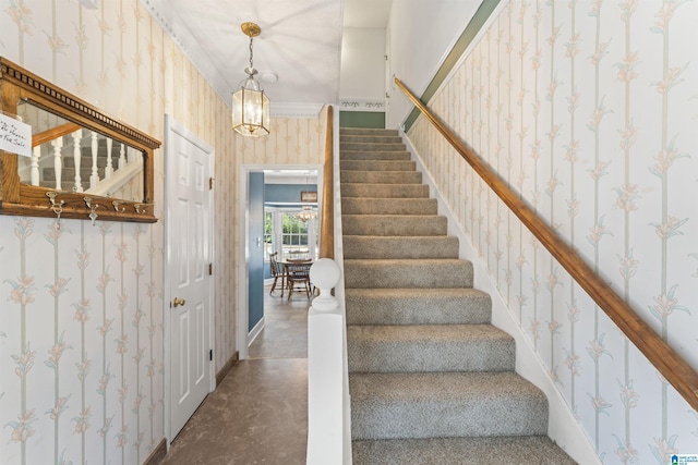 staircase with wallpapered walls, baseboards, ornamental molding, an inviting chandelier, and concrete floors