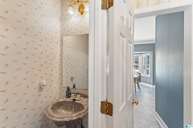 bathroom featuring wallpapered walls, baseboards, and a sink