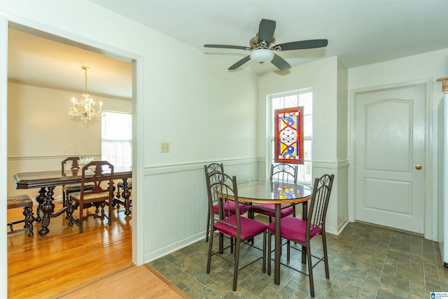 dining space with ceiling fan with notable chandelier, wood finished floors, and wainscoting