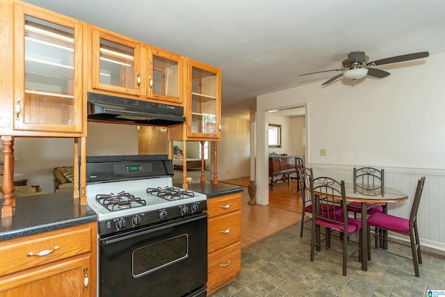 kitchen featuring dark countertops, glass insert cabinets, wainscoting, gas range, and under cabinet range hood