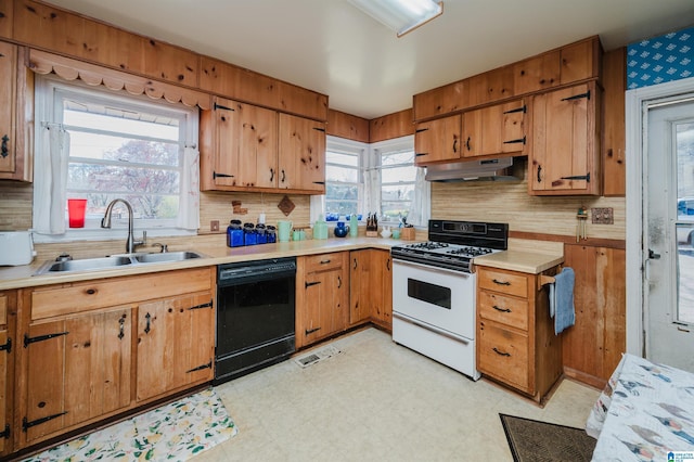 kitchen with a sink, under cabinet range hood, black dishwasher, white gas range oven, and light floors