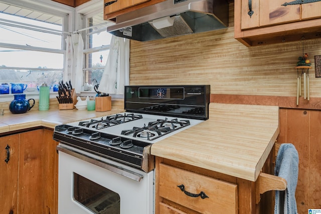 kitchen with white gas range, under cabinet range hood, and brown cabinets