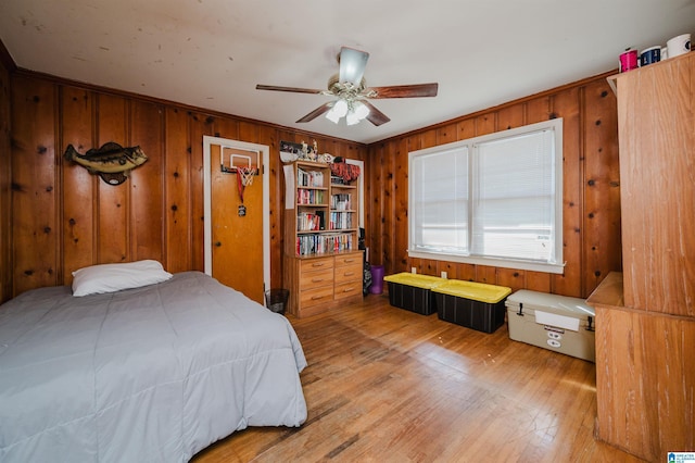 bedroom with wooden walls, ceiling fan, crown molding, and light wood finished floors