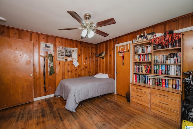 bedroom featuring a ceiling fan, wooden walls, wood finished floors, and crown molding