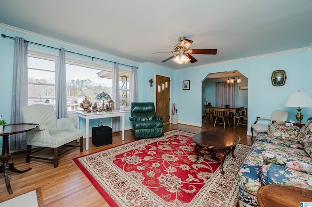 living area with crown molding, baseboards, ceiling fan with notable chandelier, wood finished floors, and arched walkways