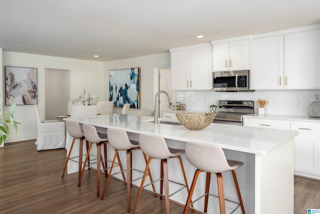 kitchen with a sink, white cabinetry, appliances with stainless steel finishes, decorative backsplash, and dark wood-style flooring