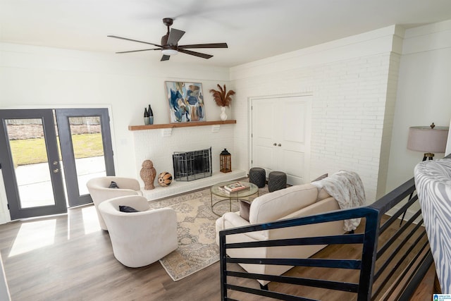 living area with brick wall, ceiling fan, a fireplace, french doors, and wood finished floors