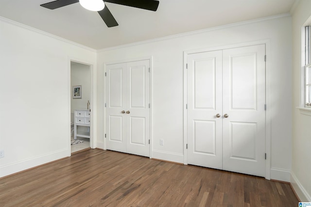 unfurnished bedroom featuring baseboards, multiple closets, wood finished floors, and crown molding