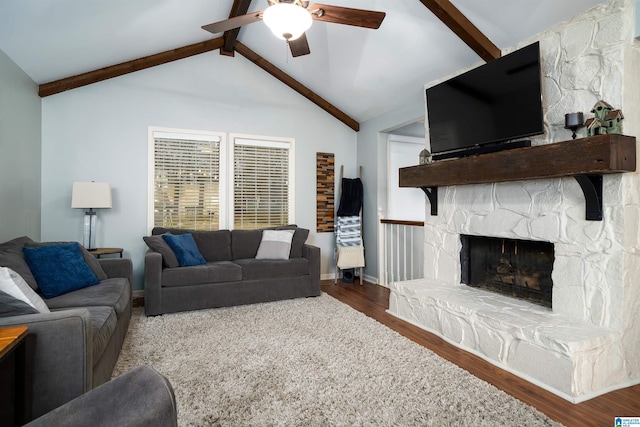 living room featuring vaulted ceiling with beams, ceiling fan, a stone fireplace, wood finished floors, and baseboards