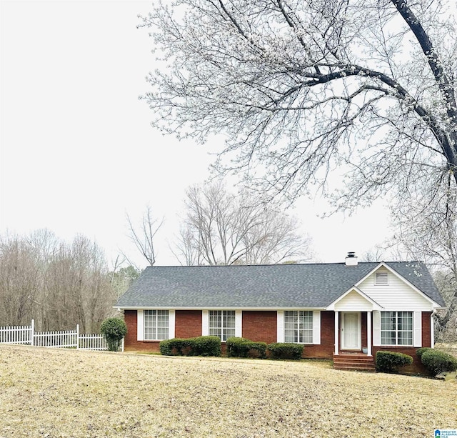 ranch-style home with fence, roof with shingles, a chimney, a front lawn, and brick siding