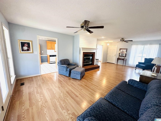 living area featuring visible vents, a ceiling fan, a textured ceiling, light wood-style floors, and a fireplace