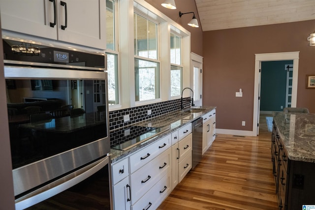 kitchen featuring dark stone counters, a sink, stainless steel appliances, white cabinetry, and tasteful backsplash