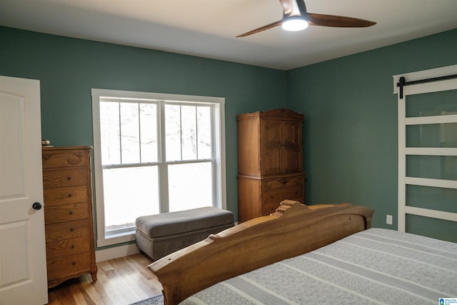 bedroom with a barn door, wood finished floors, and a ceiling fan