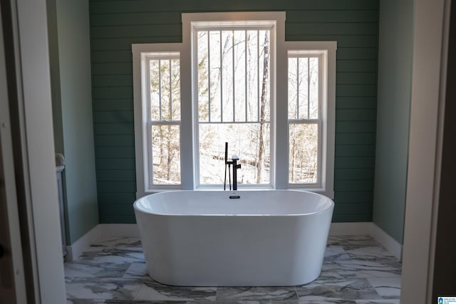 bathroom with marble finish floor, wood walls, and a freestanding bath