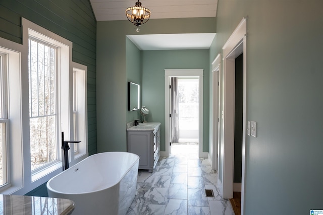 full bath featuring a freestanding tub, marble finish floor, baseboards, a chandelier, and vanity