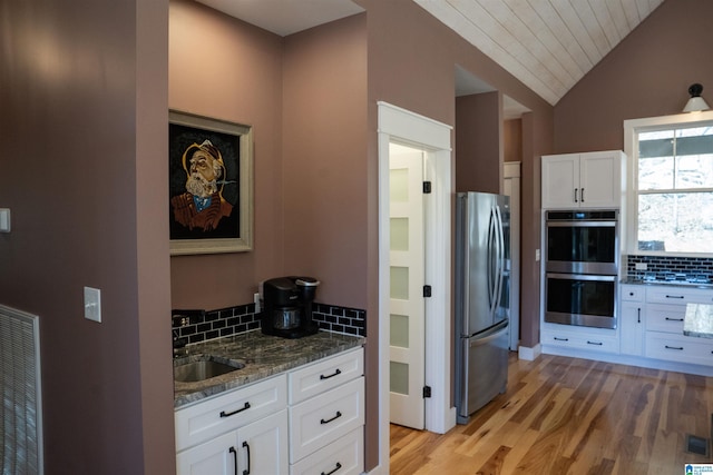 kitchen with a sink, tasteful backsplash, dark stone counters, appliances with stainless steel finishes, and white cabinets