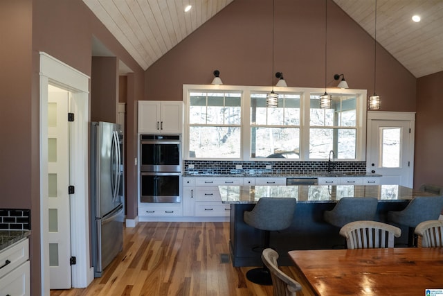 kitchen featuring tasteful backsplash, appliances with stainless steel finishes, white cabinetry, and a kitchen bar