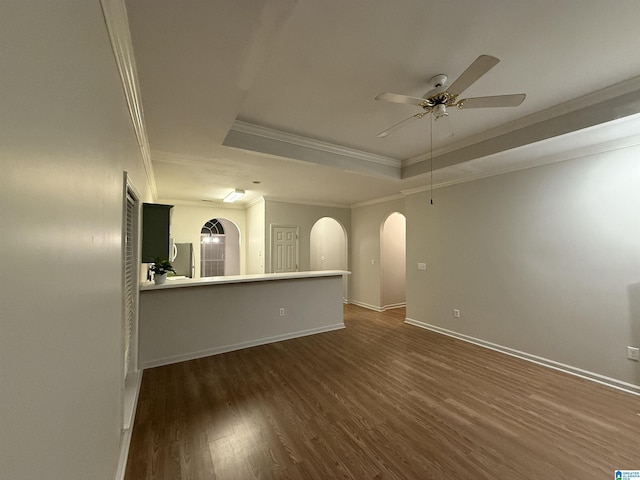 empty room with arched walkways, dark wood-type flooring, a ceiling fan, ornamental molding, and a tray ceiling