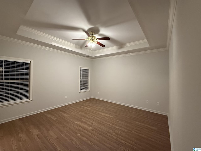 spare room with baseboards, dark wood finished floors, a ceiling fan, a tray ceiling, and crown molding