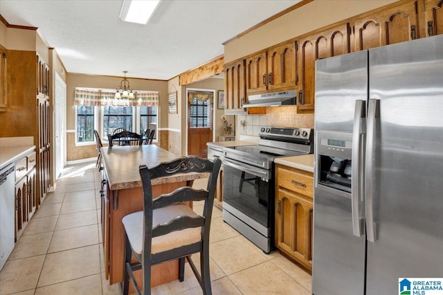 kitchen with stainless steel appliances, brown cabinetry, under cabinet range hood, and light tile patterned floors