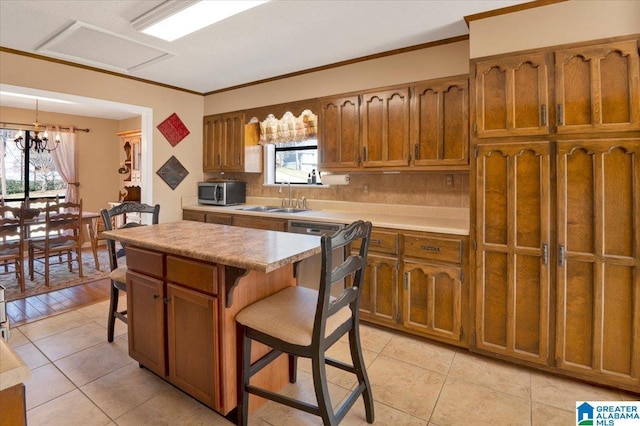 kitchen with a breakfast bar area, a sink, brown cabinetry, stainless steel microwave, and plenty of natural light