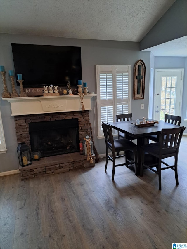 dining space featuring a fireplace, lofted ceiling, a textured ceiling, wood finished floors, and baseboards