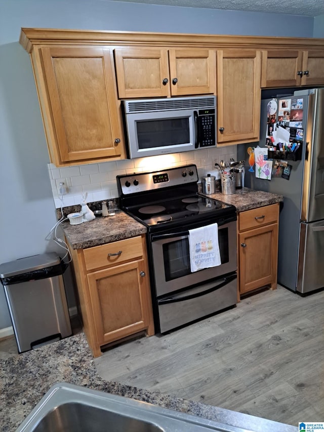 kitchen featuring dark countertops, light wood-style flooring, appliances with stainless steel finishes, and backsplash