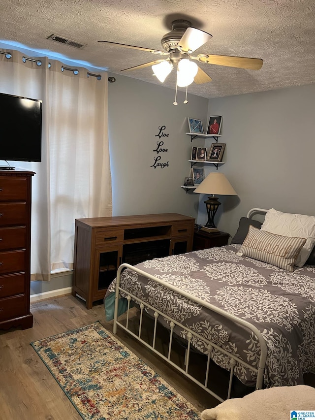 bedroom featuring a textured ceiling, wood finished floors, visible vents, and a ceiling fan