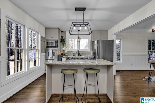 kitchen featuring stainless steel appliances, light stone countertops, a breakfast bar area, and dark wood-style floors