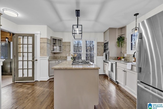 kitchen featuring a kitchen island, appliances with stainless steel finishes, dark wood-style flooring, light stone countertops, and pendant lighting