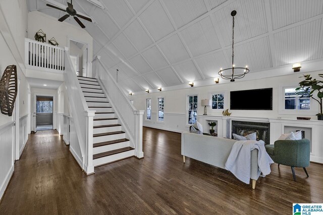 living room with a decorative wall, ceiling fan with notable chandelier, a fireplace, stairway, and dark wood finished floors