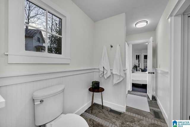 ensuite bathroom featuring a wainscoted wall, connected bathroom, visible vents, and toilet