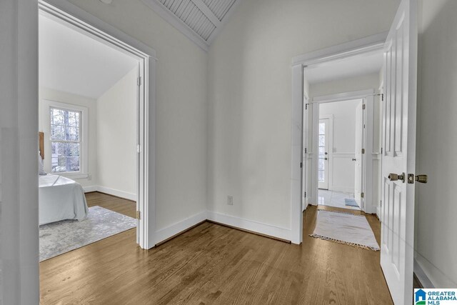 hallway with baseboards, vaulted ceiling, and wood finished floors